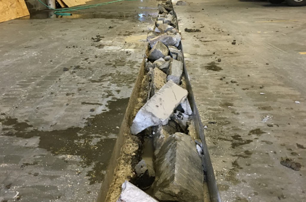 A row of broken concrete pieces lies in a long, narrow trench on the floor of an indoor construction area, highlighting ongoing Concrete Services in St Louis, MO.