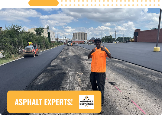 A worker in an orange shirt stands on a freshly paved road, giving two thumbs up. Construction equipment and workers are visible in the background. Text reads ASPHALT & CONCRETE SERVICES—St Louis MO! with the Asphalt Services logo.